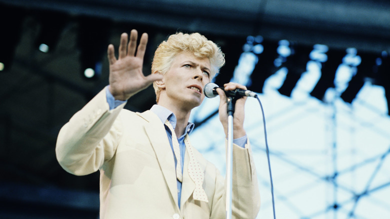 David Bowie in a cream-colored suit, performing on stage.