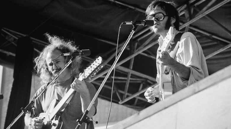 Black and white photo of David Crosby (L) and Neil Young (R) playing the guitar together on stage in 1974