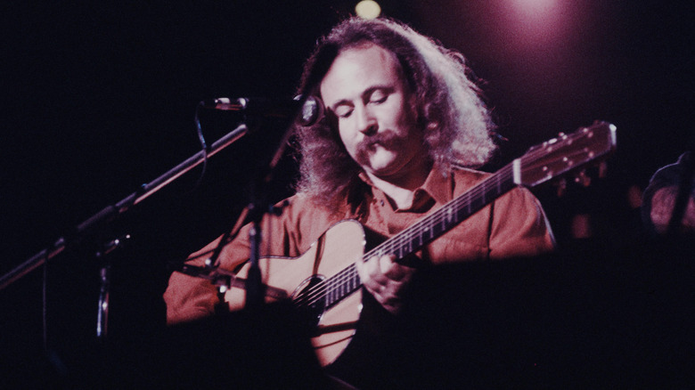 David Crosby playing the guitar on stage in Tokyo in 1975 in front of a microphone stand