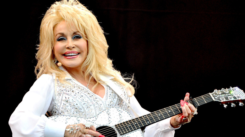 Dolly Parton smiling while playing guitar