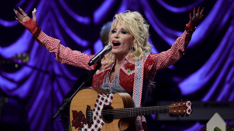 Dolly Parton on stage with guitar and arms raised