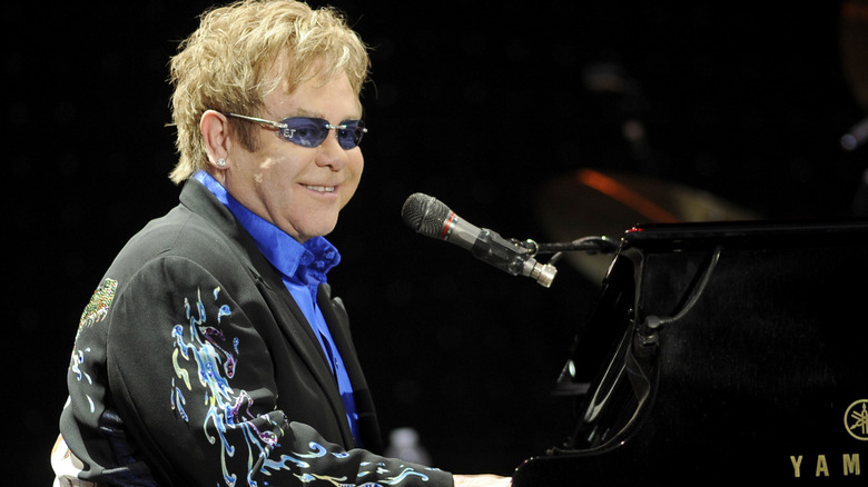 Elton John smiling at piano in blue sunglasses