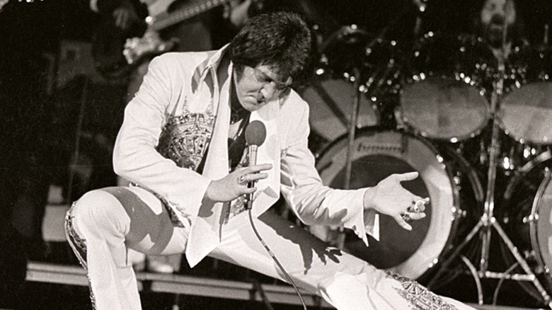 Elvis performing on stage with hand out in 1977.