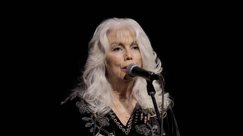 Emmylou Harris singing into a microphone in front of a black background.