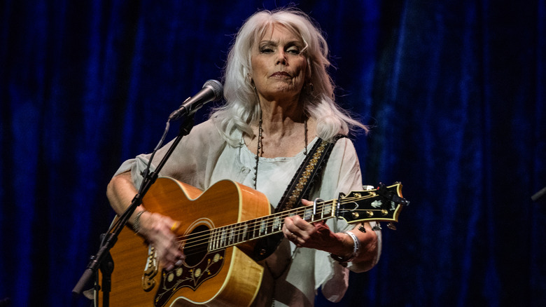 Emmylou Harris on stage, playing an acoustic guitar.