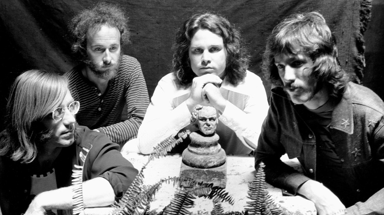 The Doors members Ray Manzarek, Robby Krieger, Jim Morrison and John Densmorer posing around a small bust statue for a portrait