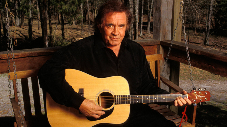 Johnny Cash sat on hanging porch bench holding an acoustic guitar