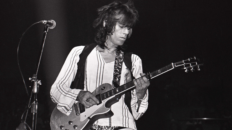 Black and white photo of Keith Richards playing the guitar on stage with the Rolling Stones wearing a striped long sleeved shirt