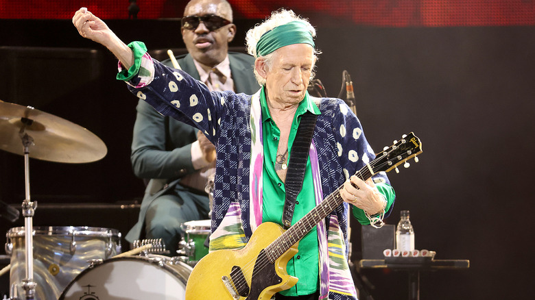 Keith Richards playing the guitar in a paterned jacket, scarf, and shiny green top while performing with the Rolling Stones in 2024