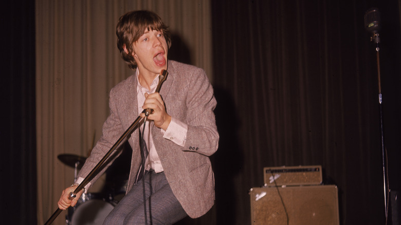 Mick Jagger crouching down singing into a microphone and holding the stand during a concert in the 1960s