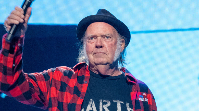 Neil Young holding up a microphone with his right hand.
