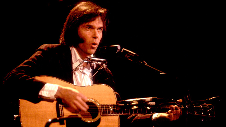 Neil Young singing and playing guitar on stage.