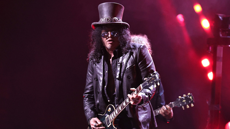 Slash playing guitar on stage in top hat and sunglasses