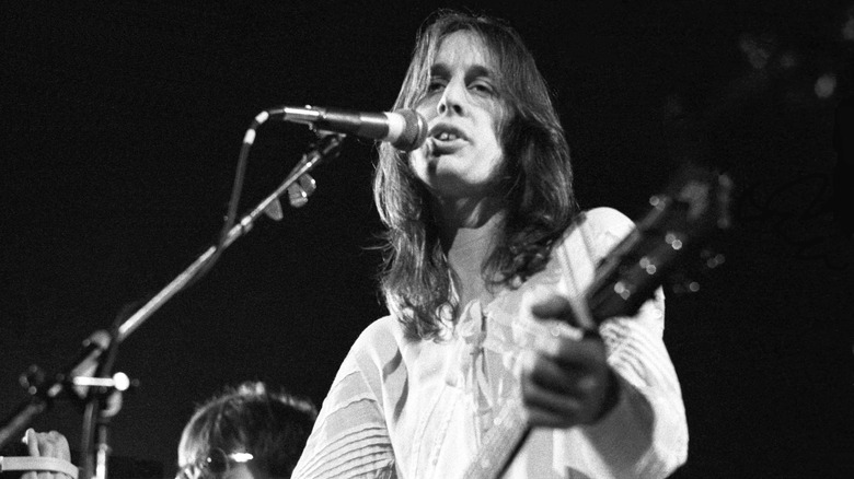 Todd Rundgren singing and playing the guitar onstage in the 70s in a white linen jumpsuit