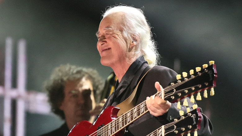 Jimmy Page on stage, smiling at the audiences while holding his two-necked guitar.
