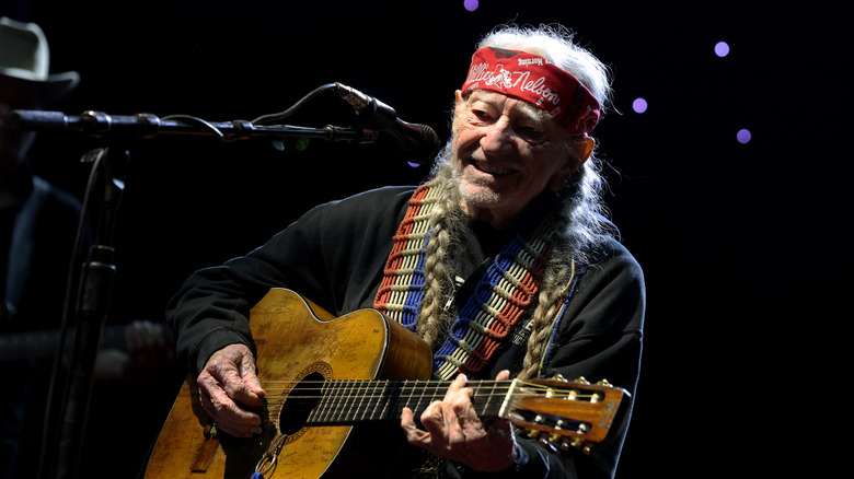 Willie Nelson smiling and playing guitar in concert