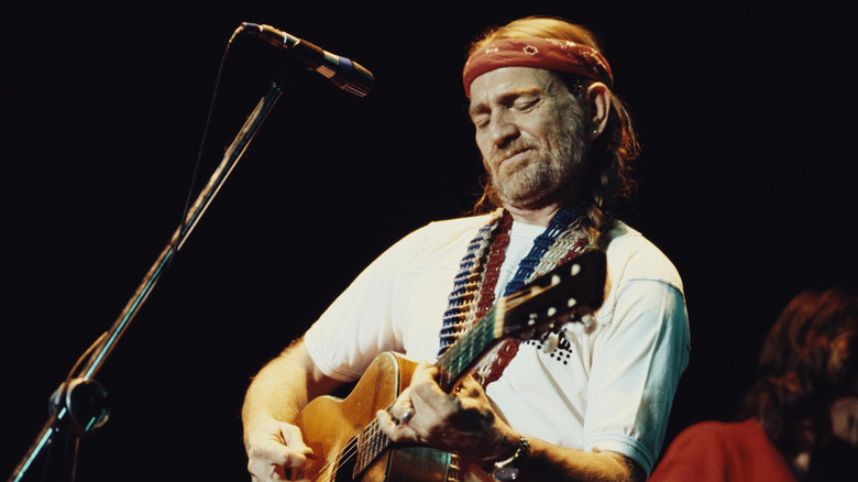 Willie Nelson playing guitar on stage with eyes closed