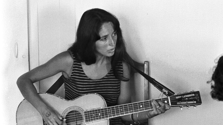 Joan Baez sitting in a chair playing guitar