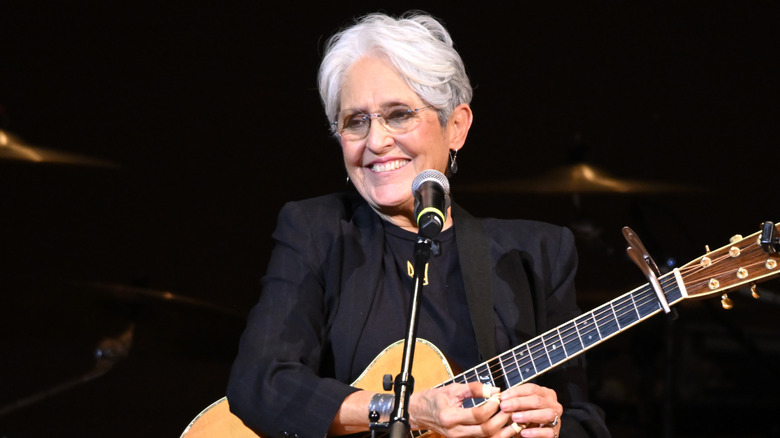 Joan Baez smiling onstage with guitar