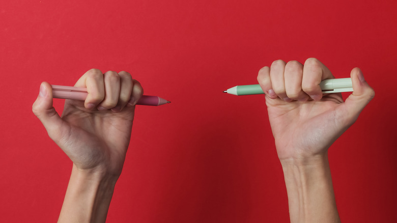 Left and right hands holding pens on red background