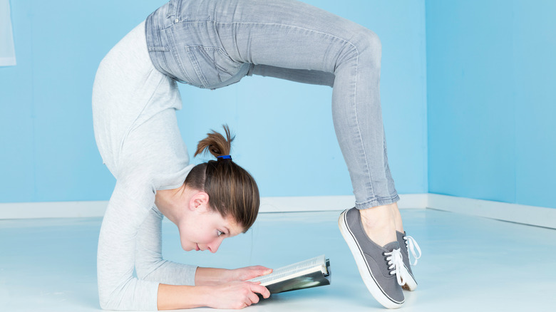 A woman reading a book while bending her legs backwards above her head