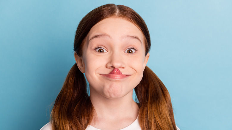 A young girl touching her tongue to her nose