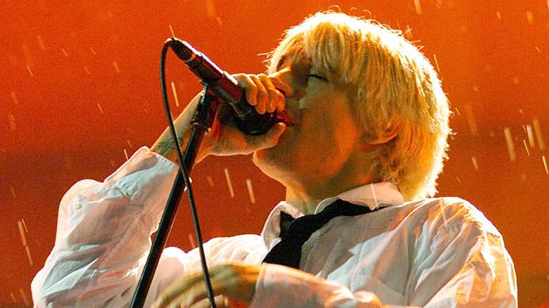Anthony Kiedis singing in white shirt on stage with red background