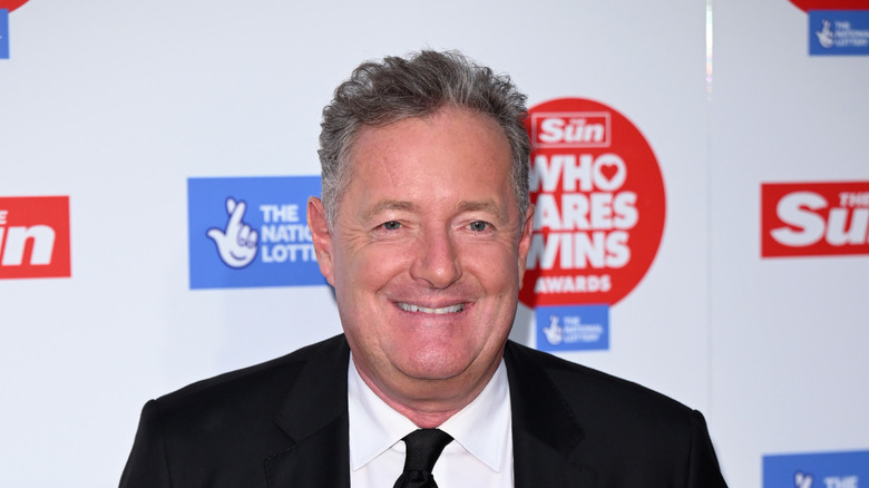 Piers Morgan grinning in suit and looking off