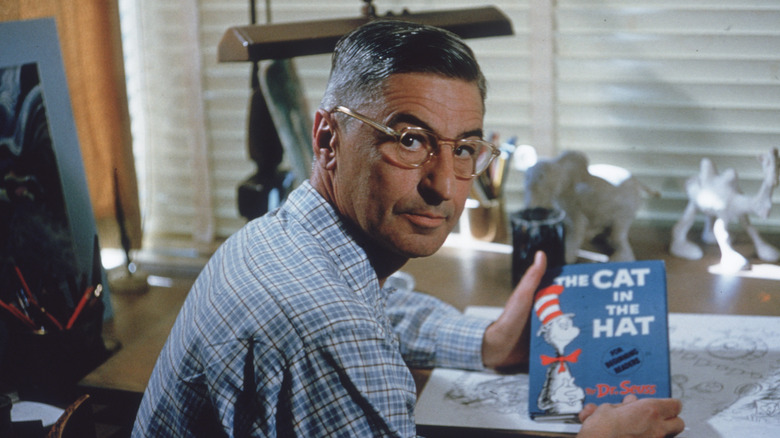 Theodor Geisel at desk holding copy of The Cat in the Hat