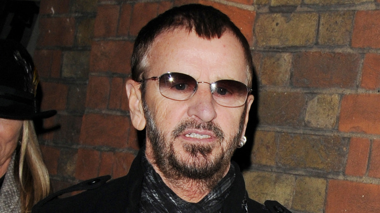 Ringo Starr grimacing in front of brick wall