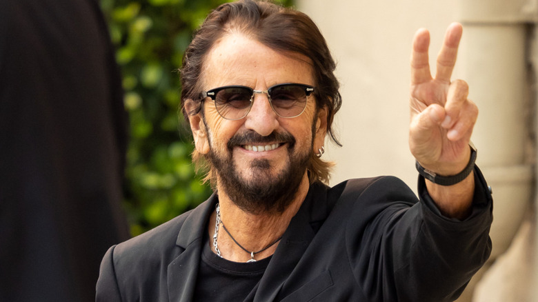 Ringo Starr smiling and flashing peace sign