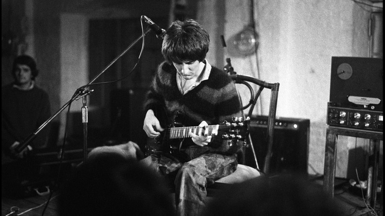 Black and white photo of Vini Reilly playing the guitar onstage in the 80s