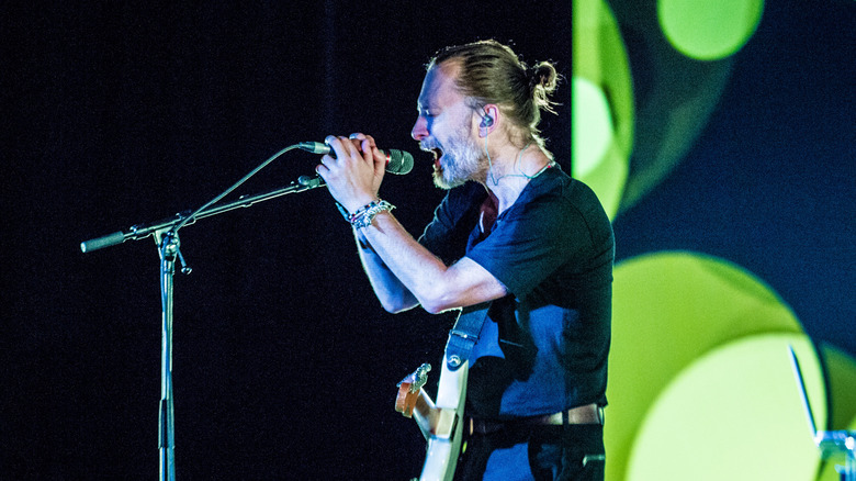 Thom Yorke holding a microphone with both hands as graphics of green circles float on stage behind him during a 2018 concert in Amsterdam