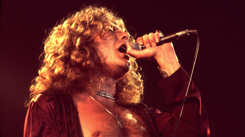 Robert Plant singing on stage in 1977 wearing a silver engraved choker, open red embroidered blouse, and a lightning rod pendant