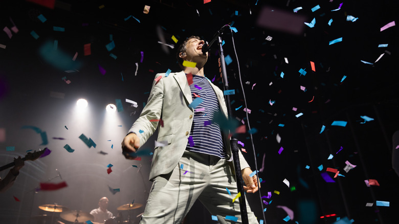 Damian Kulash of OK Go sings into a microphone on stage while rainbow confetti rains from above