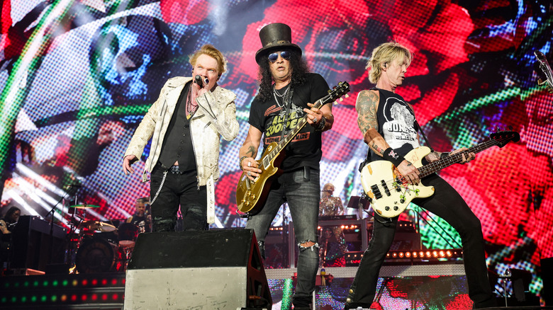 Guns 'N' Roses members Axl Rose, Slash, and Duff McKagan performing on stage.