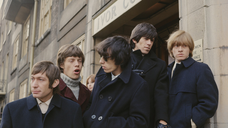 The Rolling Stones in matching coats, standing outside of a flat in London.