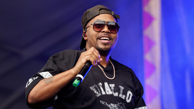 Nas performing on stage with a mic in hand, smiling.