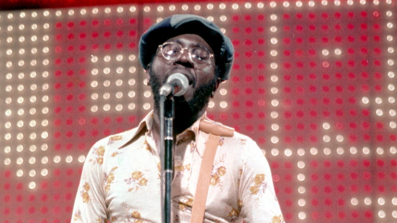 Curtis Mayfield singing on stage in glasses and flat cap