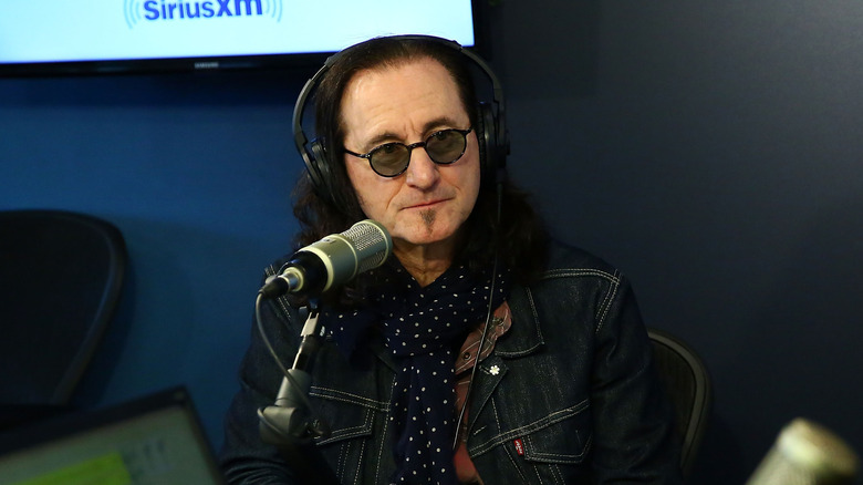 Geddy Lee of Rush seated behind a microphone at a radio station.