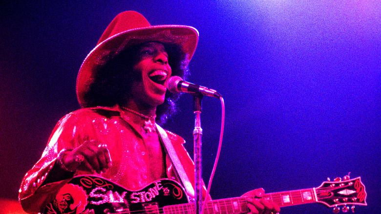 Sly Stone playing guitar and singing on stage.