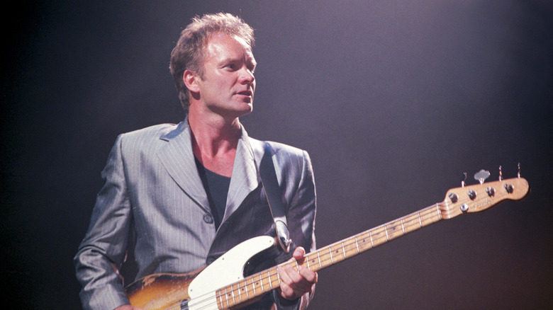 Sting wearing silver suit playing guitar on stage