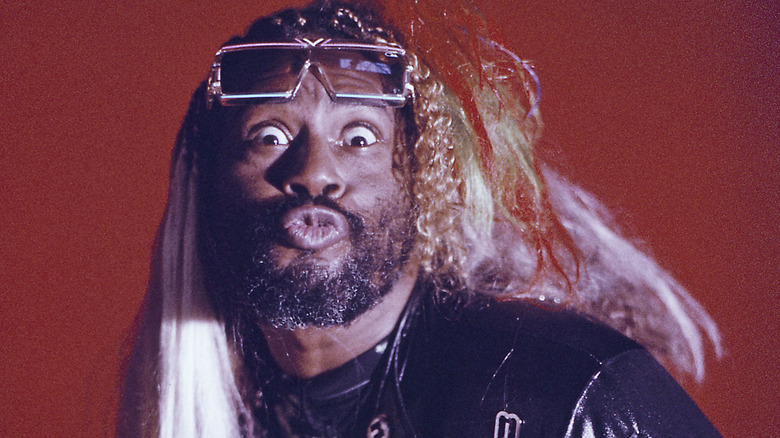 George Clinton making a funny face in a photo portrait set against a red background