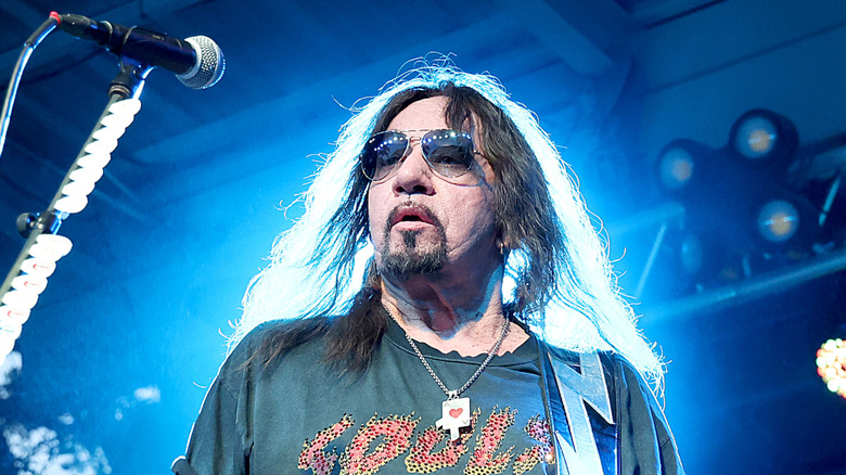 Ace Frehley wearing sunglasses long hair and beard performing on stage