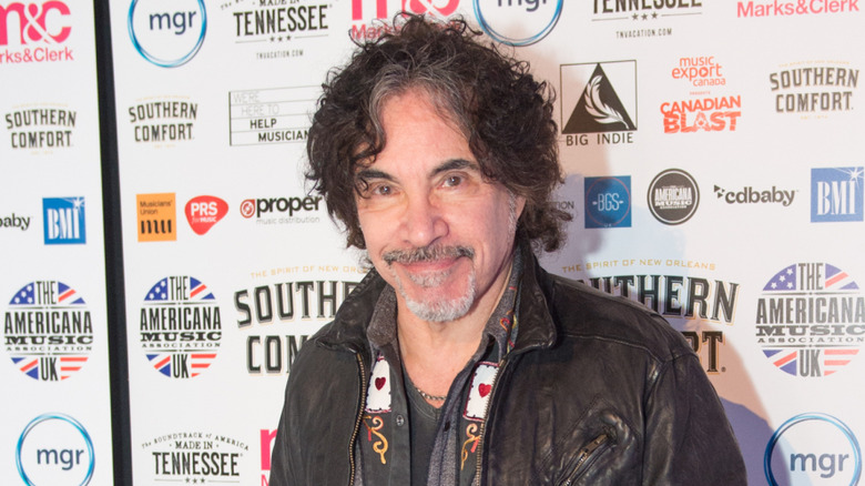 John Oates posing in front of a banner