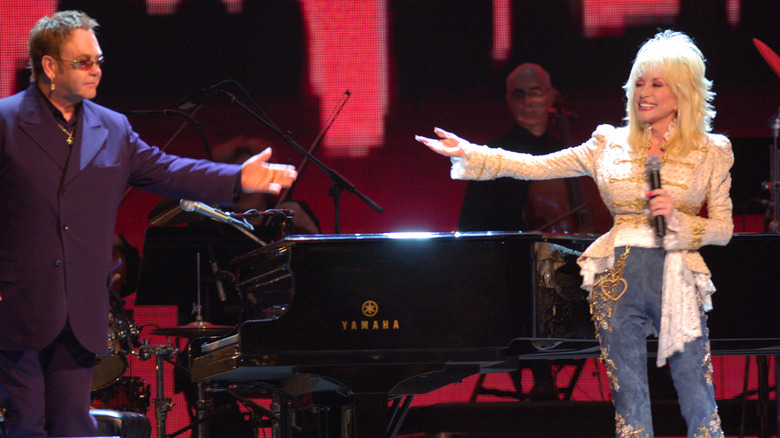 Elton John and Dolly Parton reaching their hands towards each other while performing on stage
