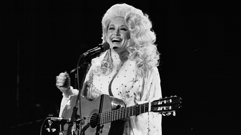 Dolly Parton smiling in a bedazzled outfit holding her guitar