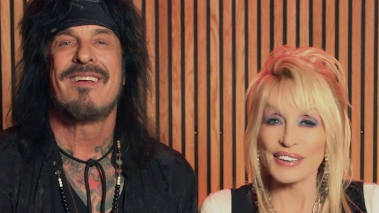 Nikki Sixx of Mötley Crüe and Dolly Parton smiling front of a wood paneled backdrop