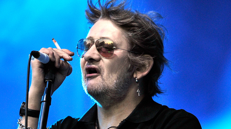 Shane McGowan singing into microphone and holding cigarette