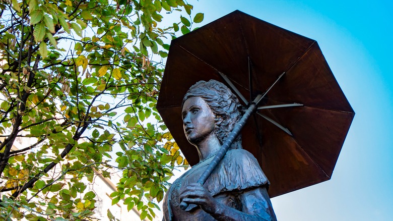 Statue of empress Elisabeth holding umbrella outside by tree
